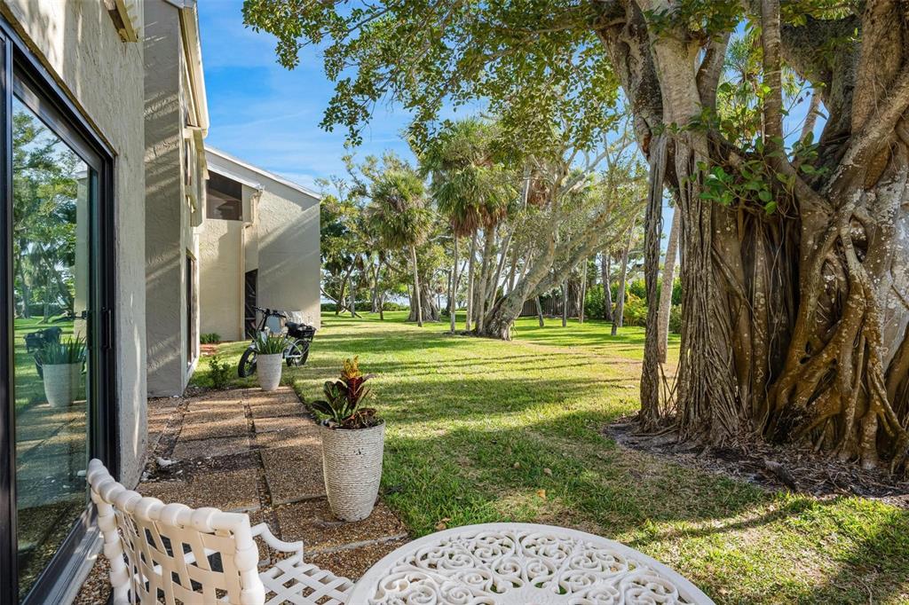 A patio with white furniture overlooks a grassy lawn shaded by large, mature trees — 5260 GULF OF MEXICO DRIVE UNIT 403, LONGBOAT KEY, FL