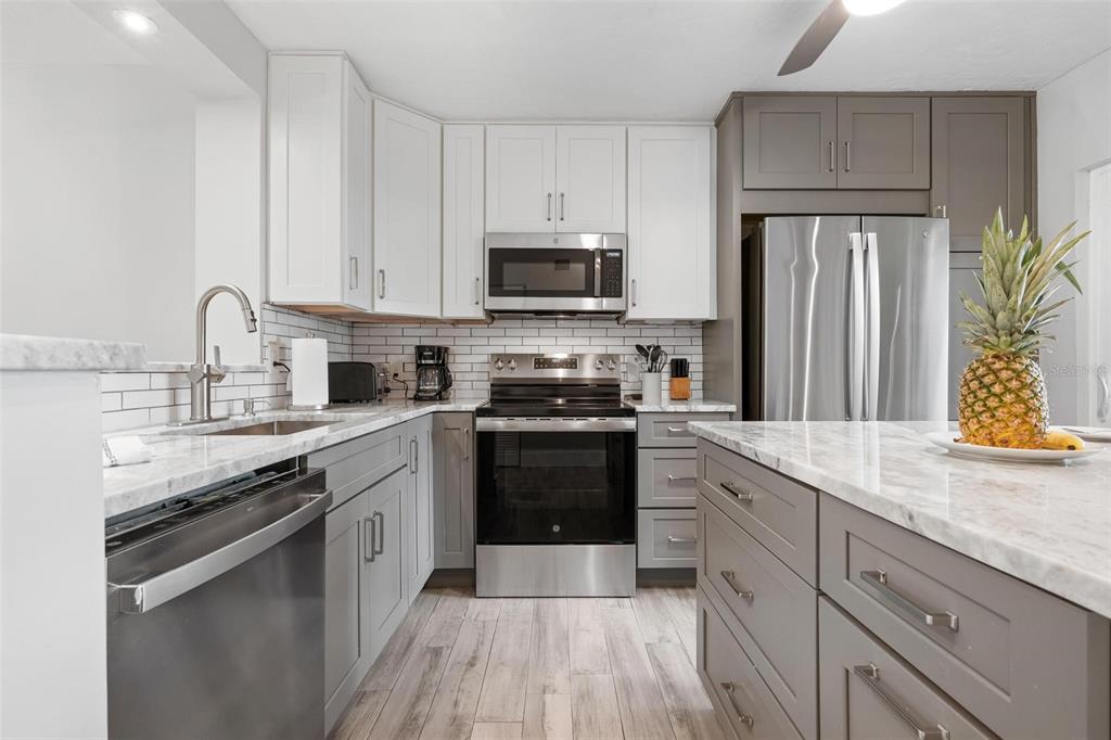 A kitchen features white upper cabinets, gray lower cabinets, stainless steel appliances, and marble countertops — 5260 GULF OF MEXICO DRIVE UNIT 403, LONGBOAT KEY, FL