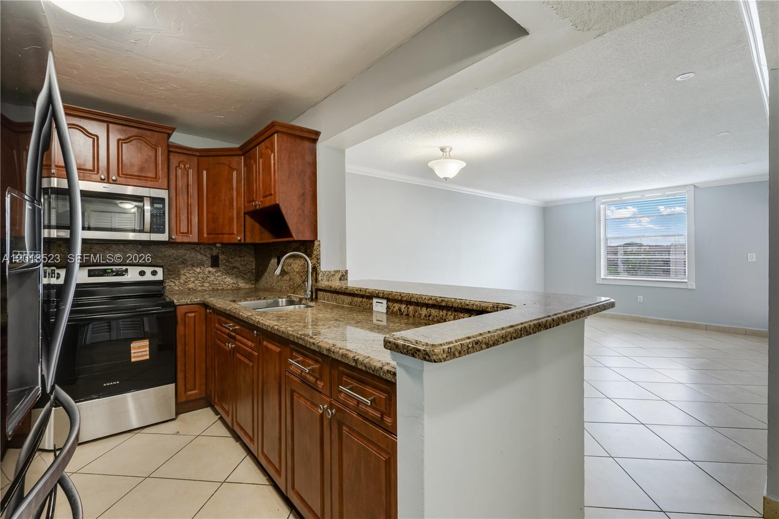 A kitchen with wood cabinets and granite countertops opens into a living area with tile — 5775 W 20th Ave # 404, Hialeah FL 33012, HIALEAH, FL