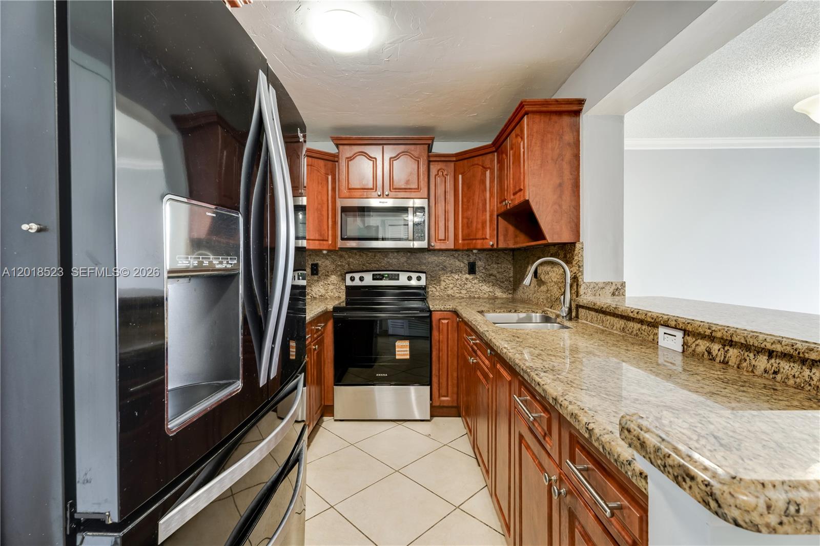 A kitchen features wood cabinets, granite countertops, and black appliances on a tiled floor — 5775 W 20th Ave # 404, Hialeah FL 33012, HIALEAH, FL