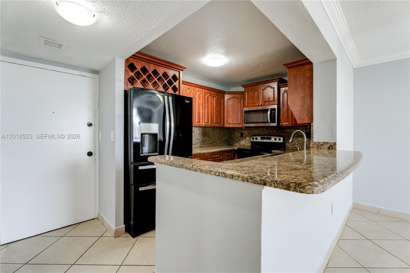 A kitchen features wood cabinets, granite countertops, a black refrigerator, and a breakfast bar — 5775 W 20th Ave # 404, Hialeah FL 33012, HIALEAH, FL