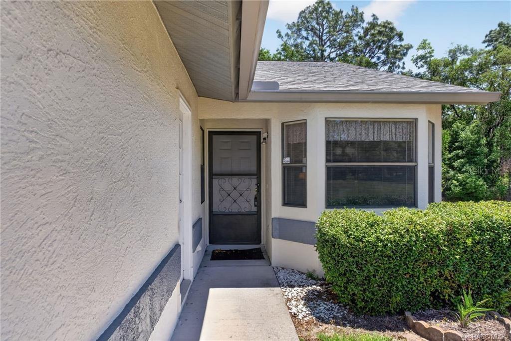A concrete walkway leads to a front door with a decorative screen door — 1857 ARROWWOOD LANE, INVERNESS, FL