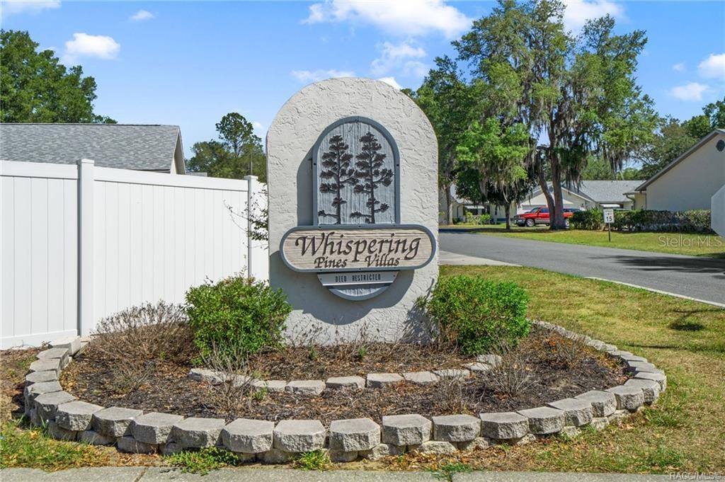 A stone monument sign for Whispering Pines Villas stands in a landscaped garden bed — 1857 ARROWWOOD LANE, INVERNESS, FL