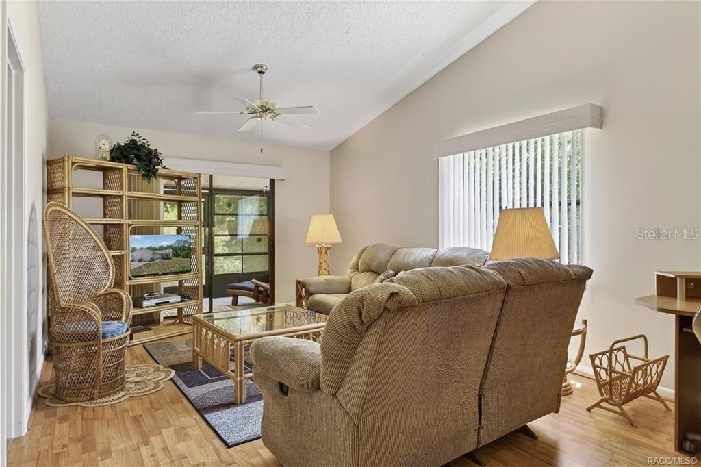 A living room features a vaulted ceiling, wood-look flooring, a rattan shelf, and a sofa — 1857 ARROWWOOD LANE, INVERNESS, FL