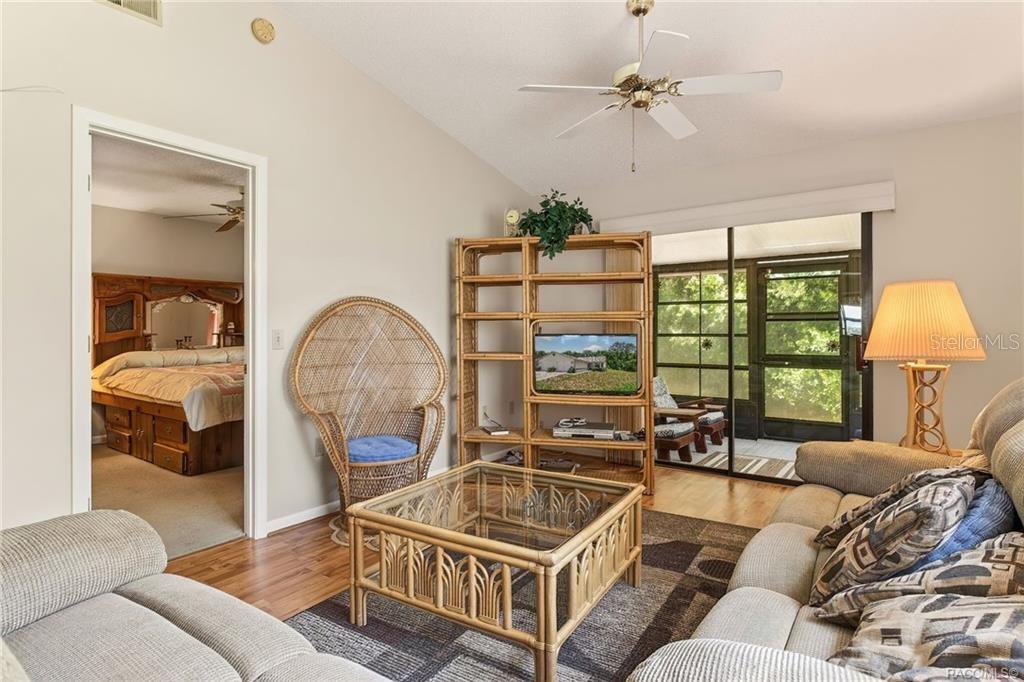A living room with a rattan coffee table, shelving unit, and view into a bedroom — 1857 ARROWWOOD LANE, INVERNESS, FL