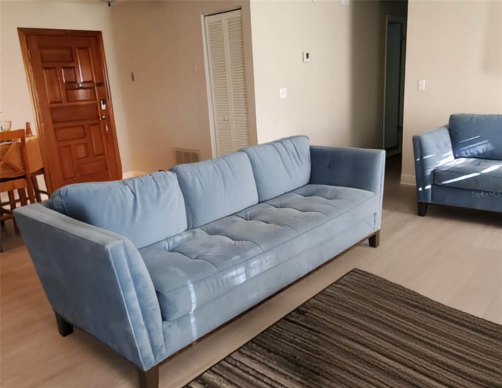A living room features a light blue tufted sofa, light wood flooring, and a brown rug — 1217 MARDRAKE ROAD, DAYTONA BEACH, FL