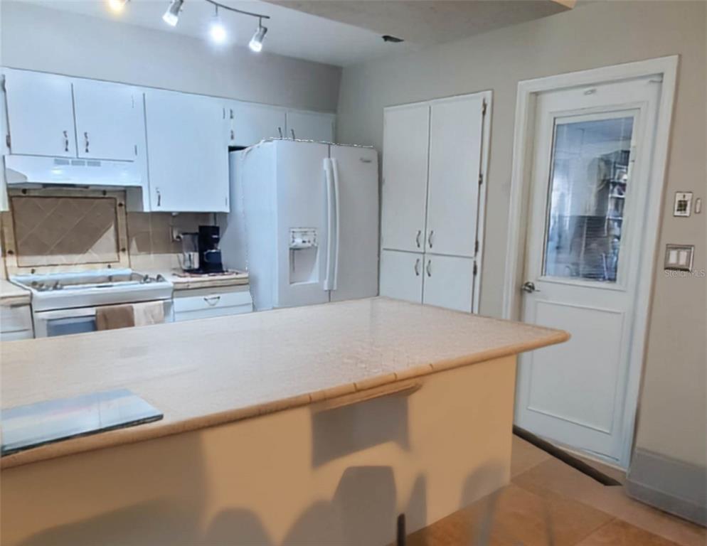 A kitchen features white cabinets, a white refrigerator, a tile-topped island, and a glass-paneled door — 1217 MARDRAKE ROAD, DAYTONA BEACH, FL