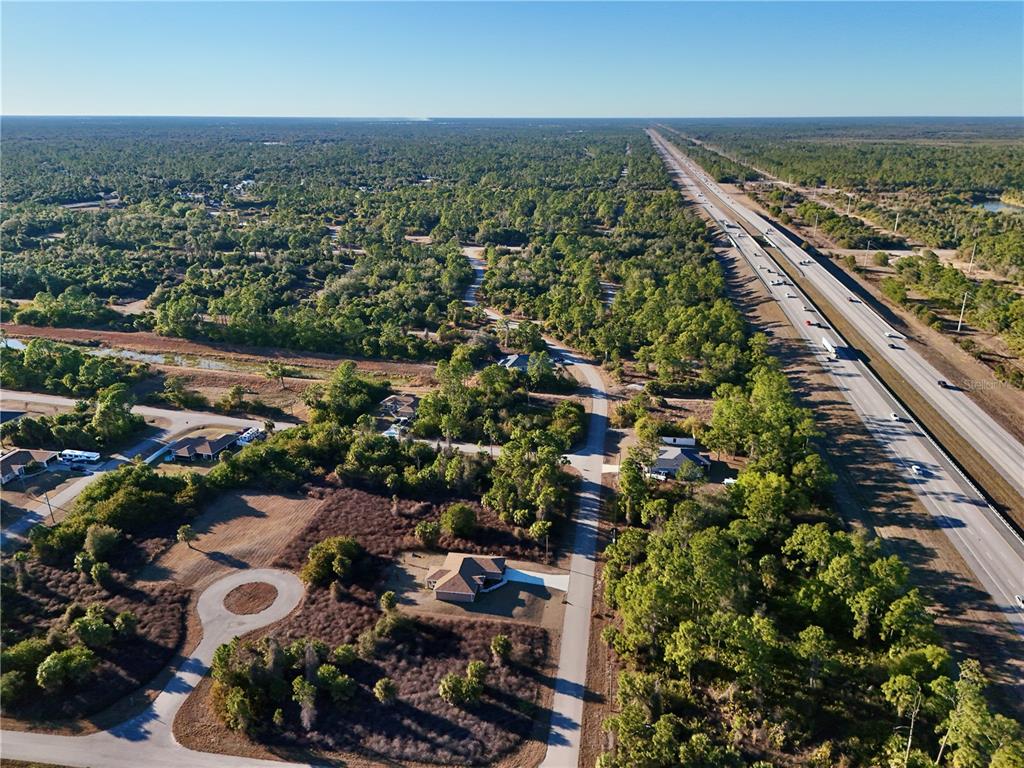 An aerial view shows a single-family home situated near a highway and dense forest — DALEWOOD CIRCLE, NORTH PORT, FL