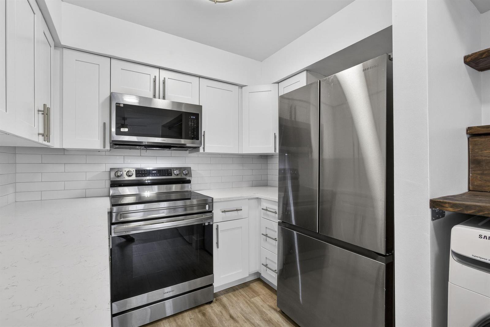 A kitchen features white cabinets, stainless steel appliances, a subway tile backsplash, and wood flooring — 9746 Nickels Boulevard, Boynton Beach FL 33436, BOYNTON BEACH, FL