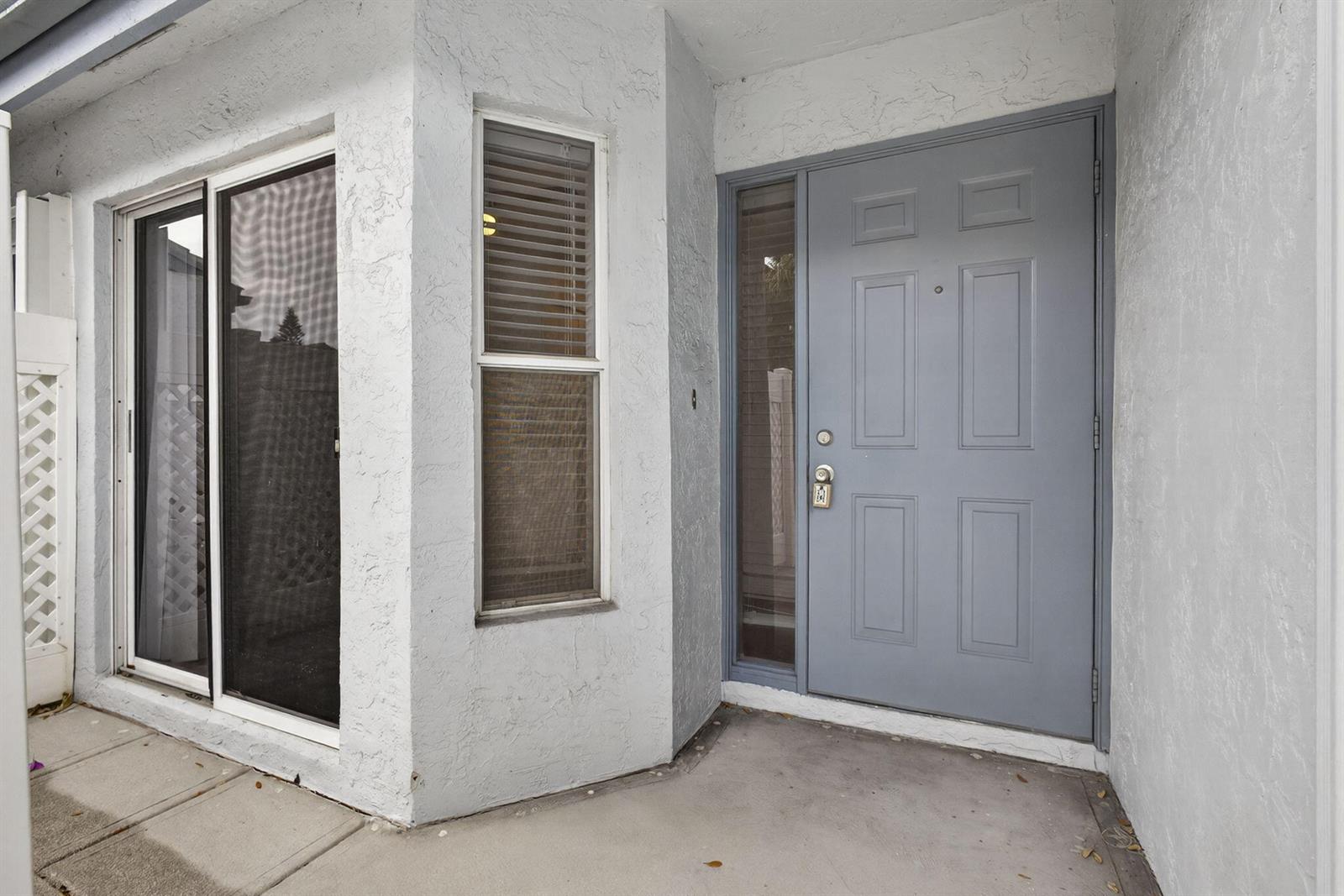 A gray front door with a side window sits next to a sliding glass door — 9746 Nickels Boulevard, Boynton Beach FL 33436, BOYNTON BEACH, FL