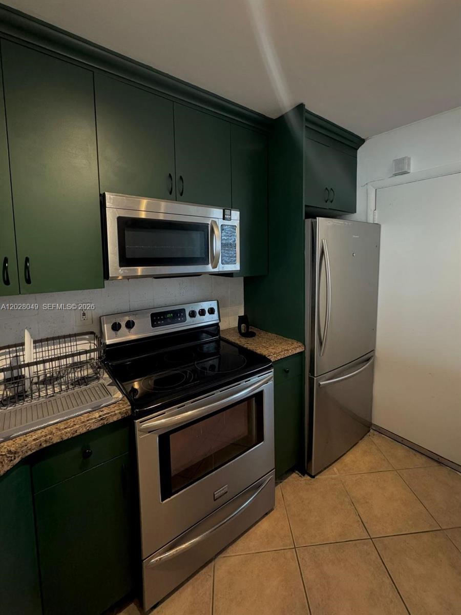 A kitchen features dark green cabinets, stainless steel appliances, and tan tile flooring — 1530 NE 191st St # 241, Miami FL 33179, MIAMI, FL