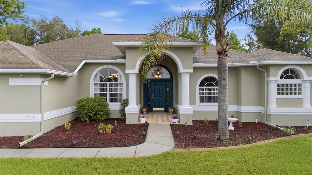 A single-story house with a beige stucco exterior, arched windows, and a dark blue front door — 3410 IRONDALE AVENUE, SPRING HILL, FL