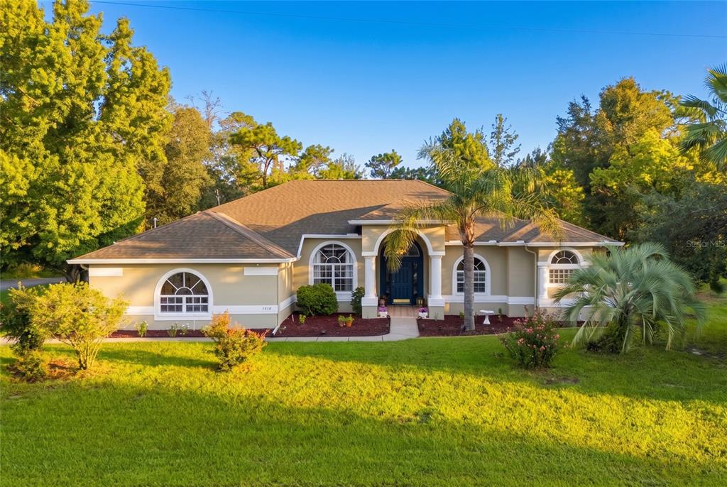 A single-story house with a tan exterior, arched windows, and a palm tree in front — 3410 IRONDALE AVENUE, SPRING HILL, FL