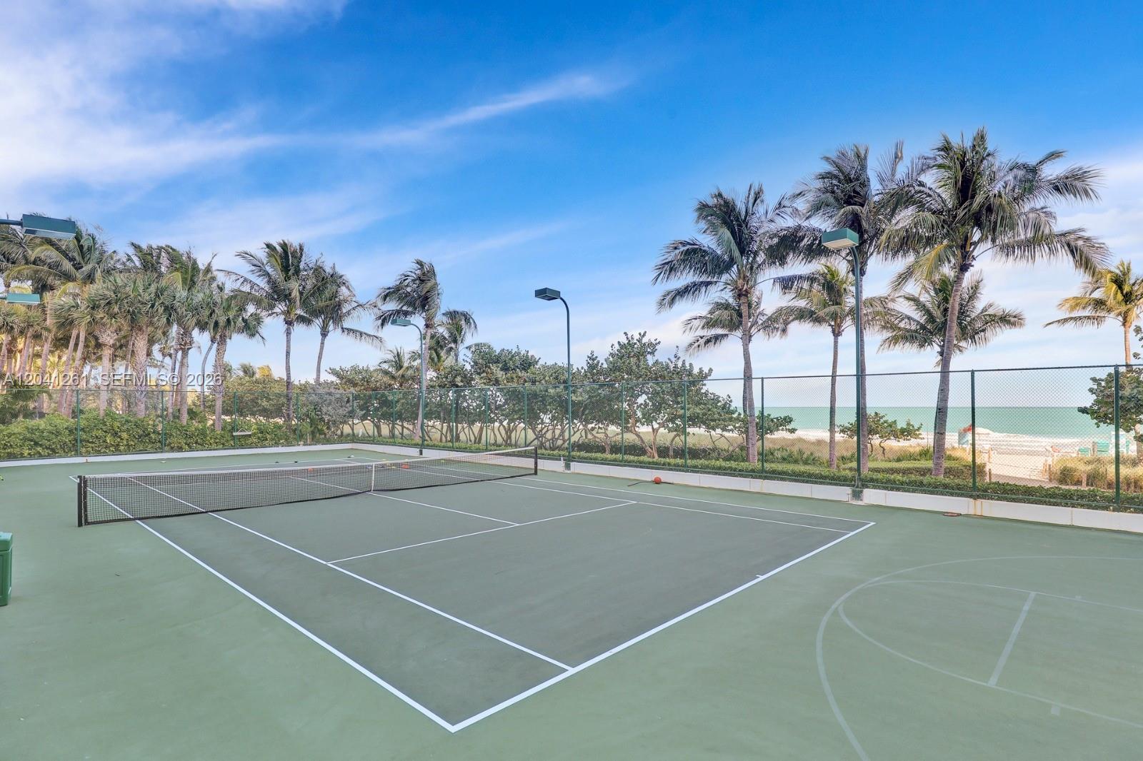 A tennis court with a net is situated outdoors near palm trees and the ocean — 9601 Collins Ave # 507, Bal Harbour FL 33154, BAL HARBOUR, FL