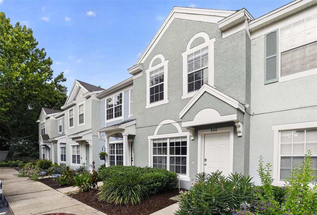A row of multi-story townhomes with gray stucco facades and white trim under a blue sky — 866 VINELAND PLACE, LAKE MARY, FL