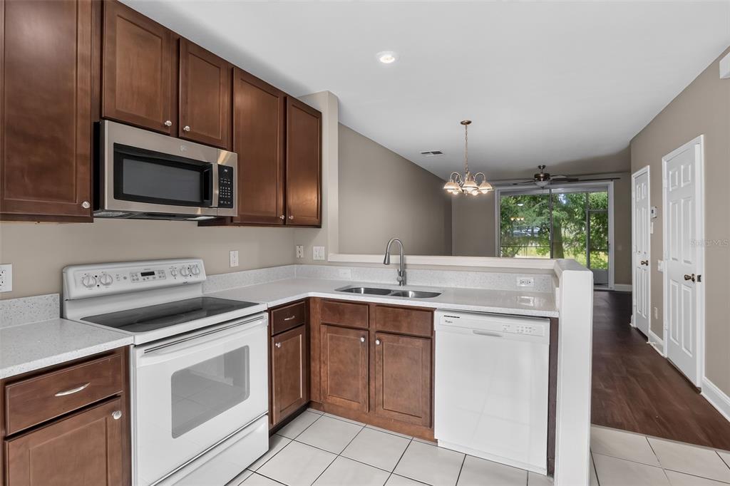 A kitchen with dark wood cabinets, white appliances, and a pass-through window to the dining area — 866 VINELAND PLACE, LAKE MARY, FL