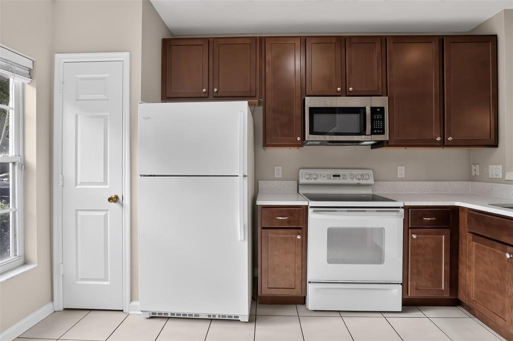 A kitchen features dark wood cabinets, white appliances, and light-colored tile flooring — 866 VINELAND PLACE, LAKE MARY, FL