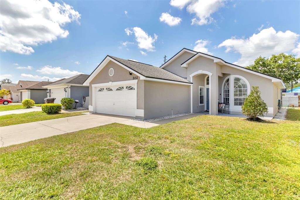 A single-story house with a beige exterior, a two-car garage, and a front lawn — 202 BAY MEADOW DRIVE, KISSIMMEE, FL