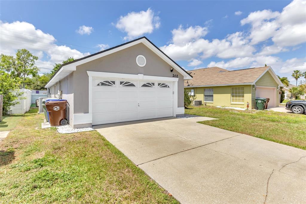 A gray house with a white garage door and a concrete driveway under a blue sky — 202 BAY MEADOW DRIVE, KISSIMMEE, FL