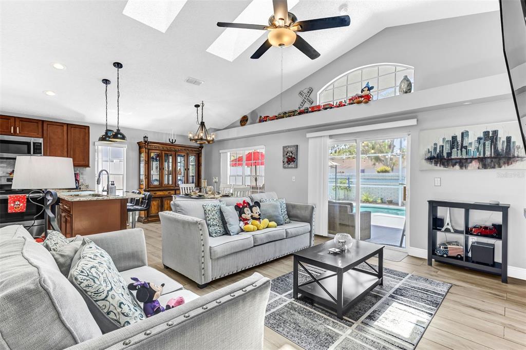 A living room with a vaulted ceiling, gray sofas, and an open kitchen area — 202 BAY MEADOW DRIVE, KISSIMMEE, FL