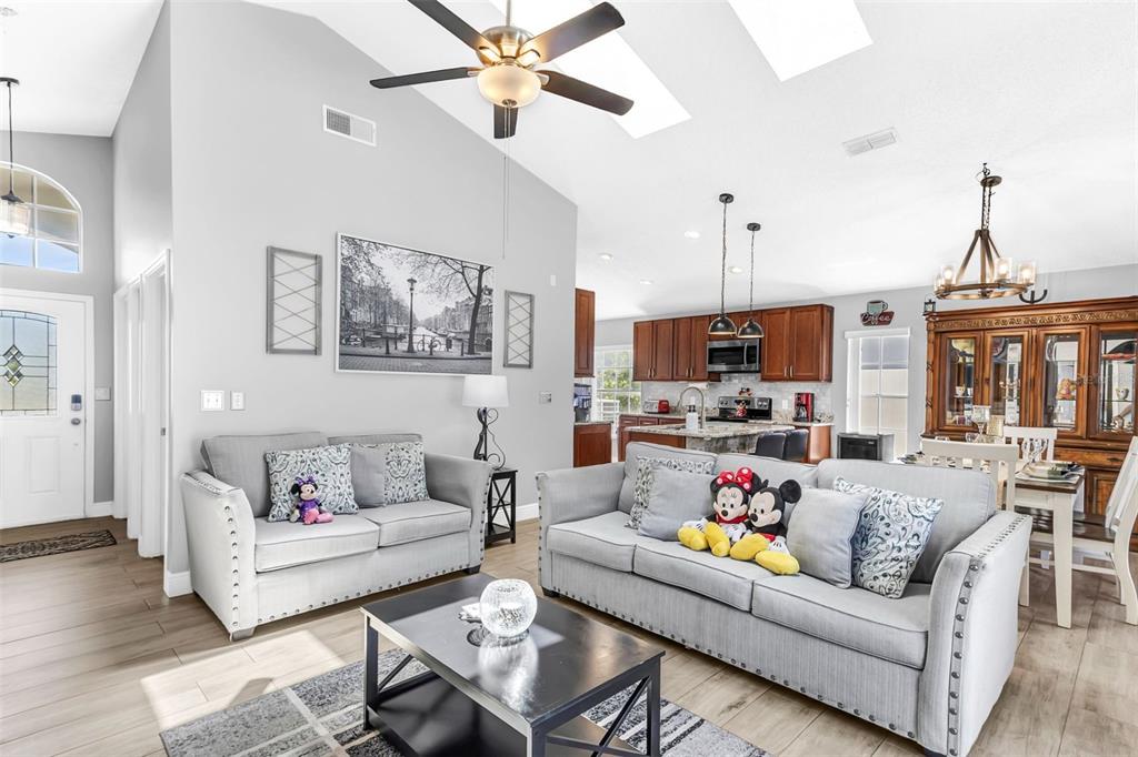An open-concept living room and kitchen featuring gray sofas, a coffee table, and wood cabinetry — 202 BAY MEADOW DRIVE, KISSIMMEE, FL