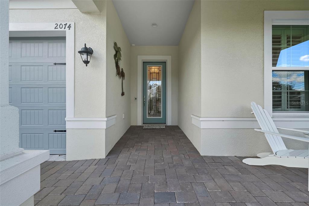 A paved front porch features a light blue door, a garage, and a white chair — 2074 FLORA PASS PLACE, KISSIMMEE, FL