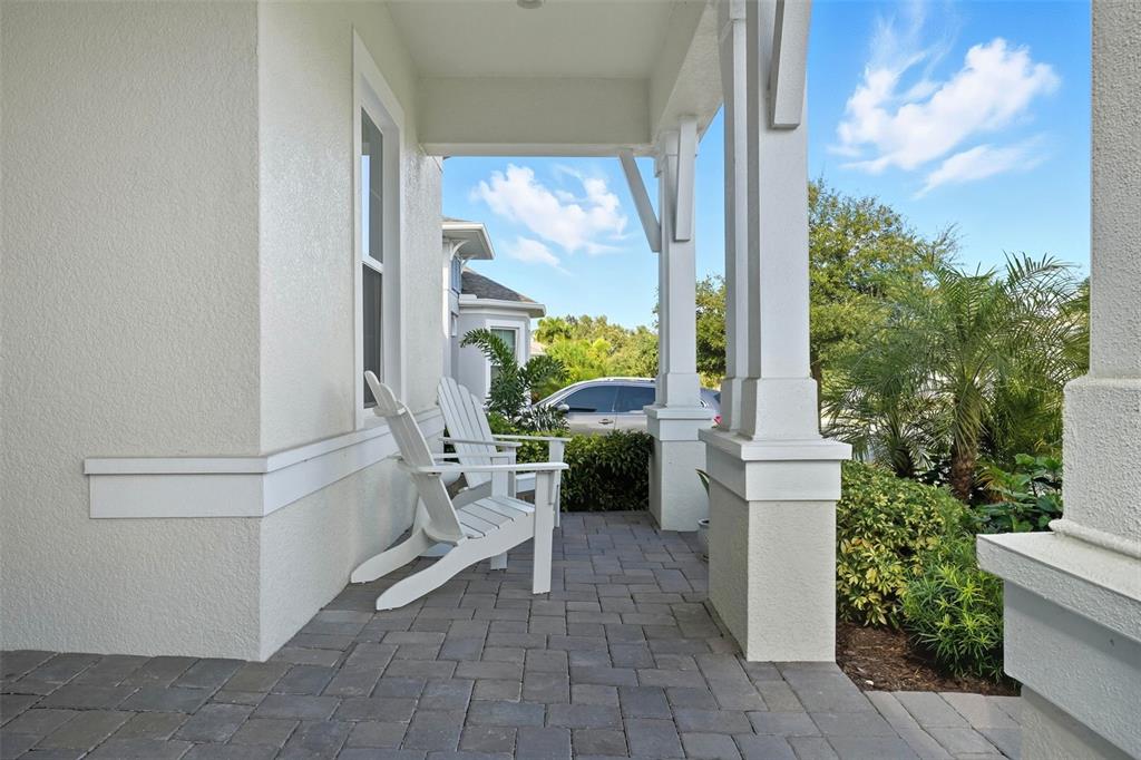 A covered front porch features white Adirondack chairs and gray paver flooring — 2074 FLORA PASS PLACE, KISSIMMEE, FL