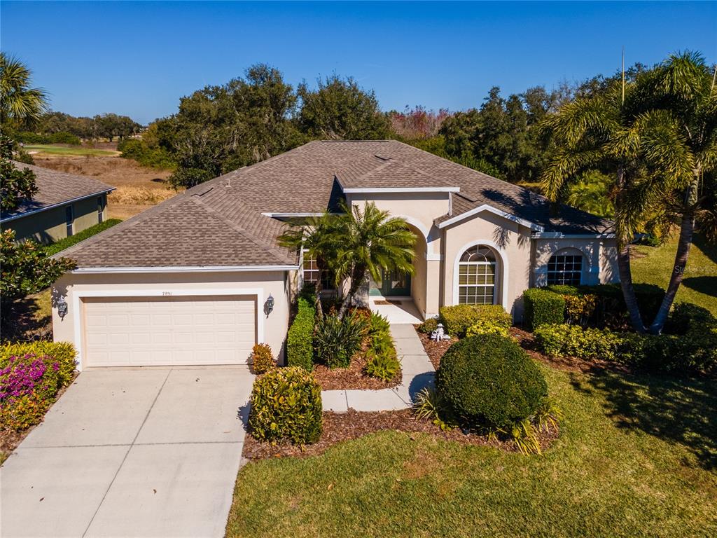 A single-story suburban house with a tan stucco exterior, a two-car garage, and landscaped yard — 7891 KAVANAGH COURT, SARASOTA, FL