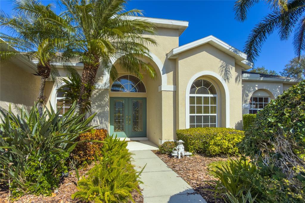 A beige house exterior features a teal double front door, arched windows, and palm trees — 7891 KAVANAGH COURT, SARASOTA, FL