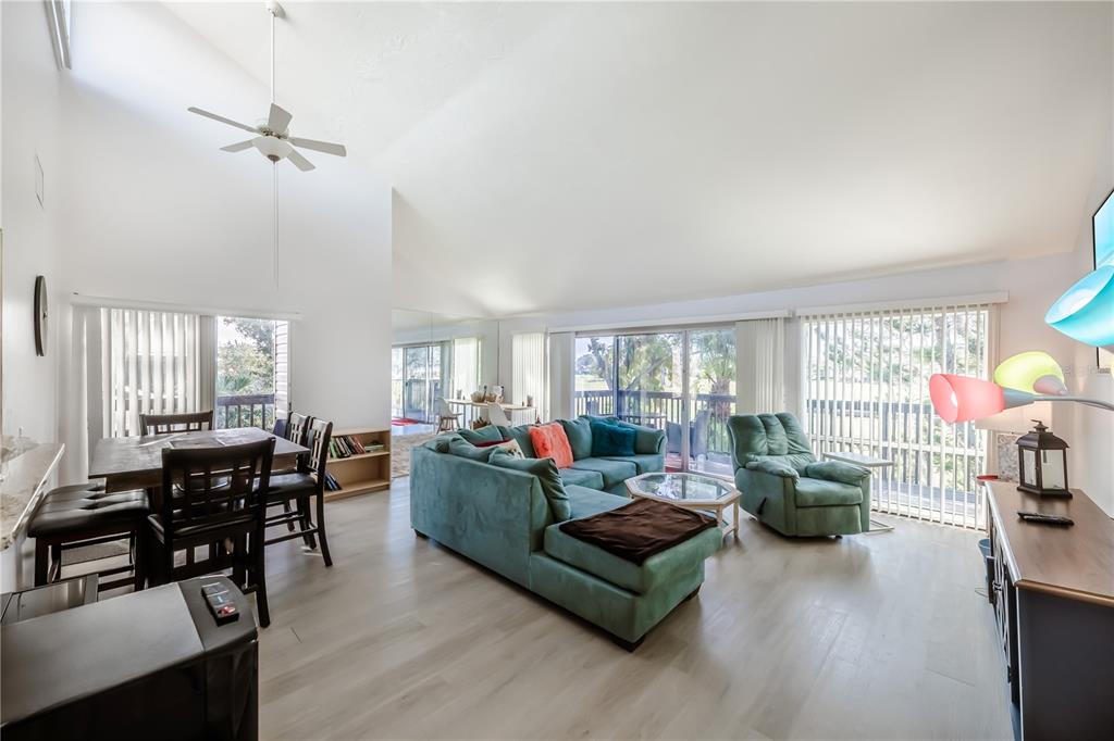 A living and dining area features vaulted ceilings, light wood flooring, and a teal sectional sofa — 722 WHITE PINE TREE ROAD UNIT 82, VENICE, FL