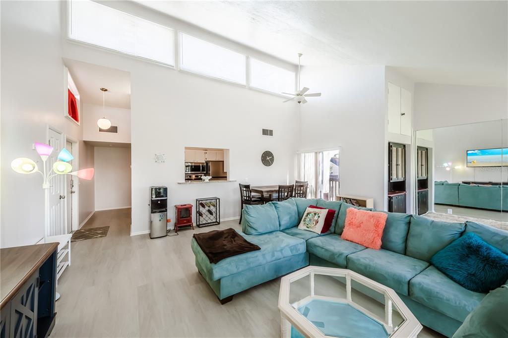 A living room features a teal sectional sofa, vaulted ceilings, and a pass-through kitchen window — 722 WHITE PINE TREE ROAD UNIT 82, VENICE, FL
