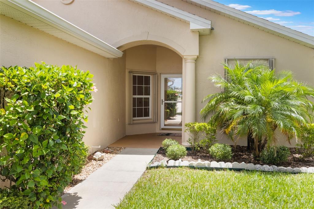 A concrete walkway leads to the arched entryway of a beige house with landscaping — 464 LAKE SUZANNE DRIVE, LAKE WALES, FL