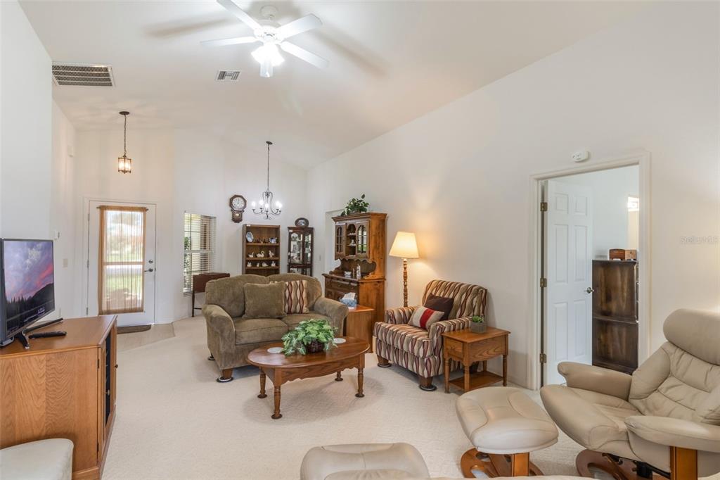 A living room features a vaulted ceiling, beige carpeting, a sofa, armchairs, and wood furniture — 464 LAKE SUZANNE DRIVE, LAKE WALES, FL