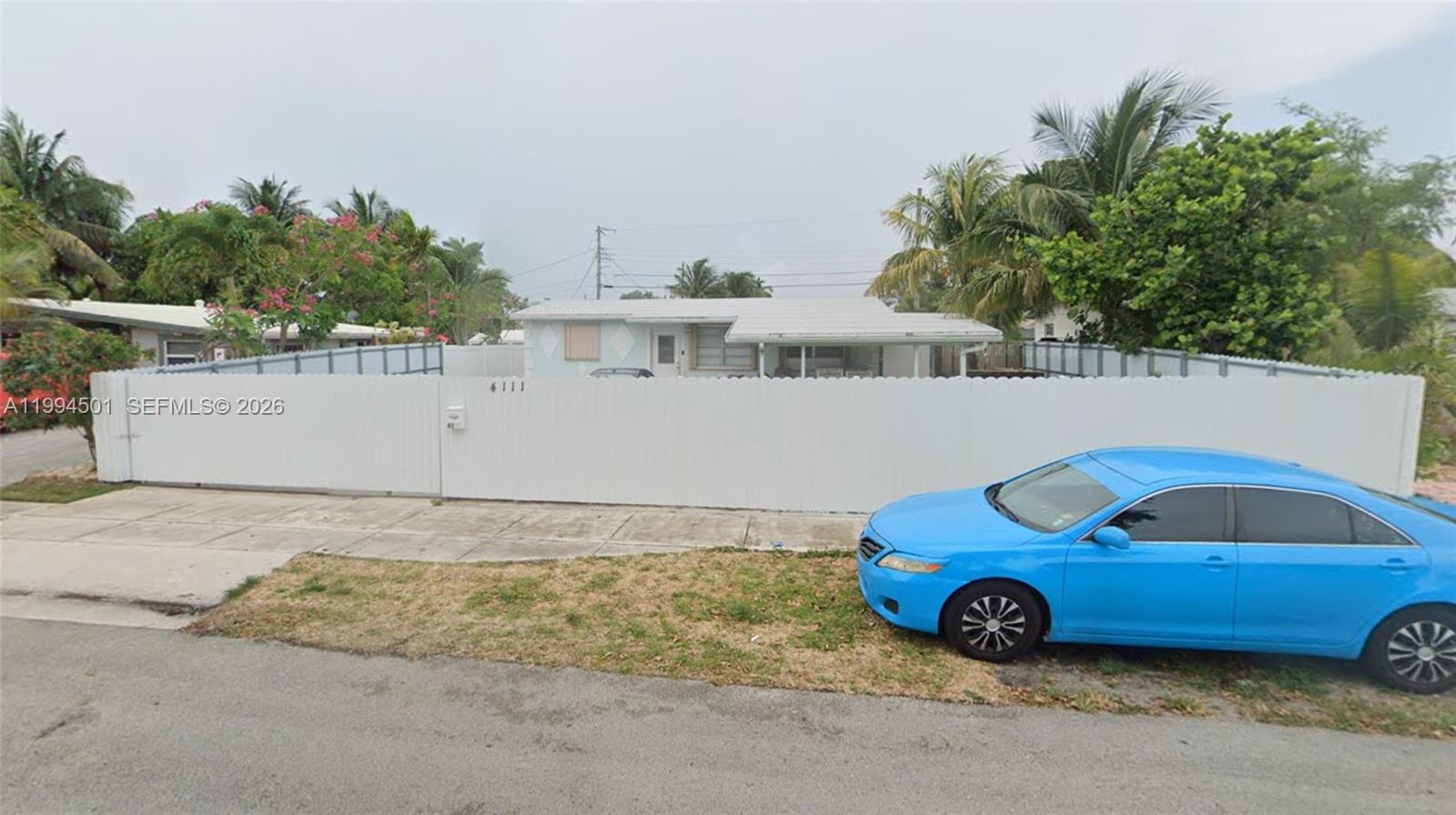 A single-story house is enclosed by a tall white fence with a blue car parked nearby — 4111 NW 10th Ter, Oakland Park FL 33309, OAKLAND PARK, FL