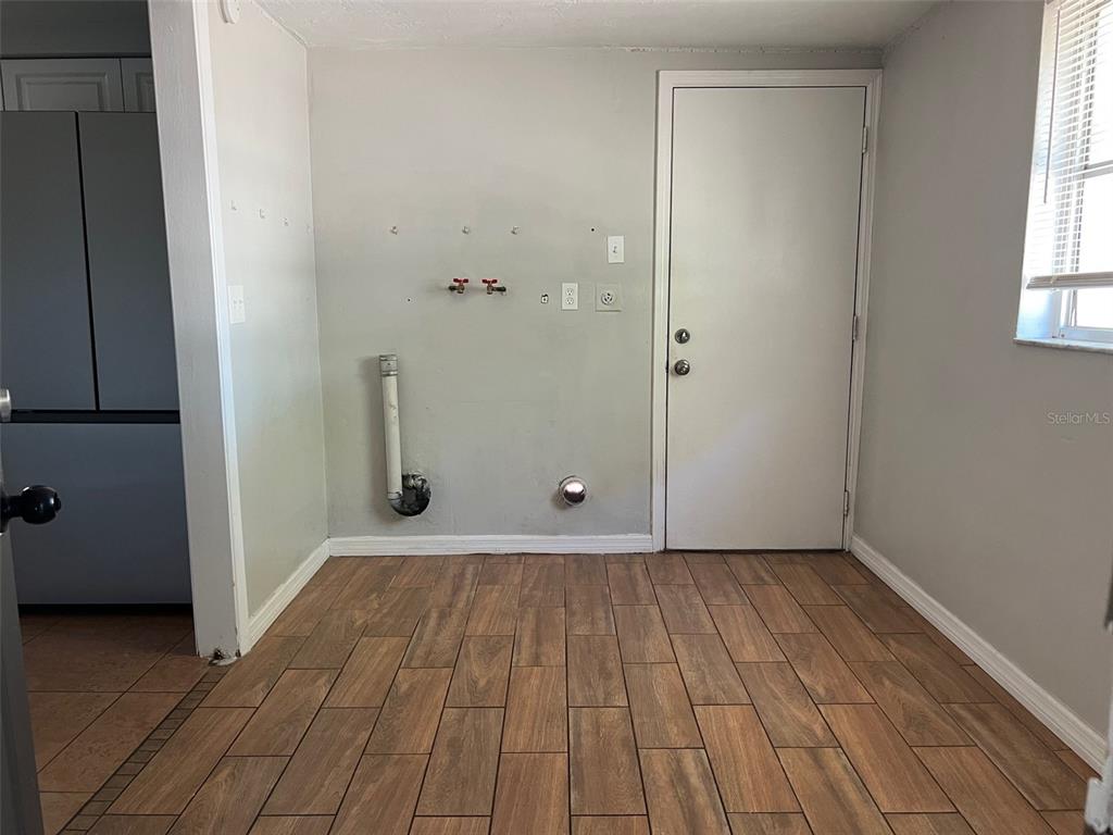 A laundry room with wood-look tile flooring, wall-mounted utility hookups, and a white exterior door — 7835 ARBORDALE DRIVE, PORT RICHEY, FL