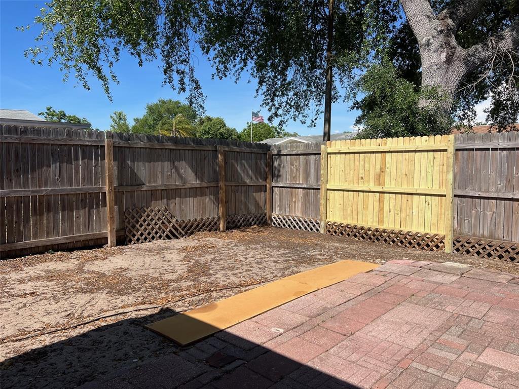 A backyard features a brick patio, a sandy area, and a wooden privacy fence — 7835 ARBORDALE DRIVE, PORT RICHEY, FL