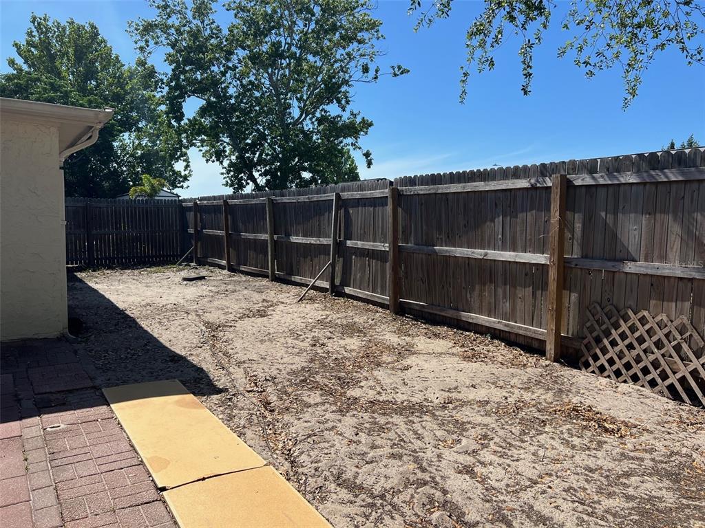 A backyard features a paved patio, sandy ground, and a wooden privacy fence — 7835 ARBORDALE DRIVE, PORT RICHEY, FL