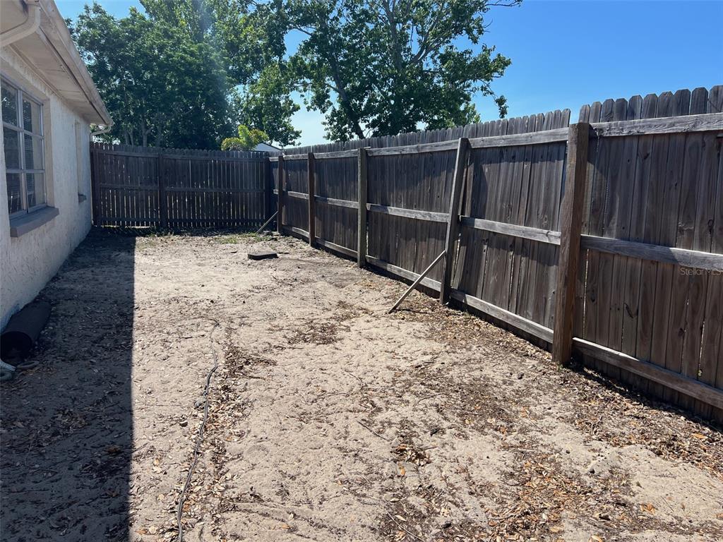 A sandy backyard area features a wooden privacy fence and the side of a house — 7835 ARBORDALE DRIVE, PORT RICHEY, FL