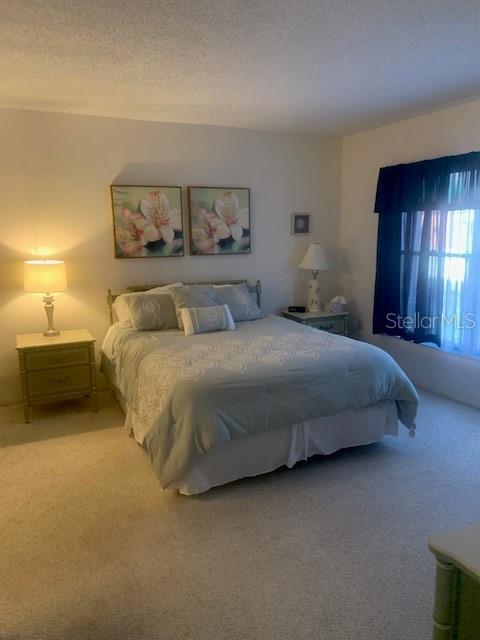 A bedroom features a bed with a light blue comforter, two framed floral prints, and curtains — 1000 BENJAMIN FRANKLIN DRIVE UNIT 205, SARASOTA, FL