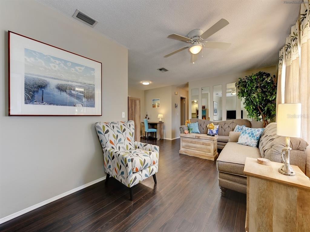 A living room features dark wood flooring, a patterned armchair, and a beige sofa — 301 AVENIDA MADERA UNIT B, SARASOTA, FL