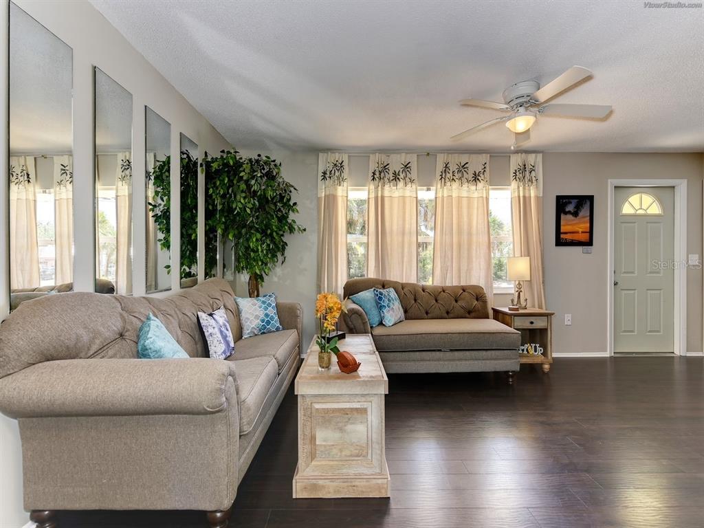 A living room features a beige sofa, a tufted chaise, wood flooring, and mirrored wall panels — 301 AVENIDA MADERA UNIT B, SARASOTA, FL