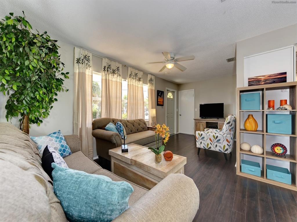 A living room features dark wood flooring, two sofas, a patterned armchair, and a shelving unit — 301 AVENIDA MADERA UNIT B, SARASOTA, FL