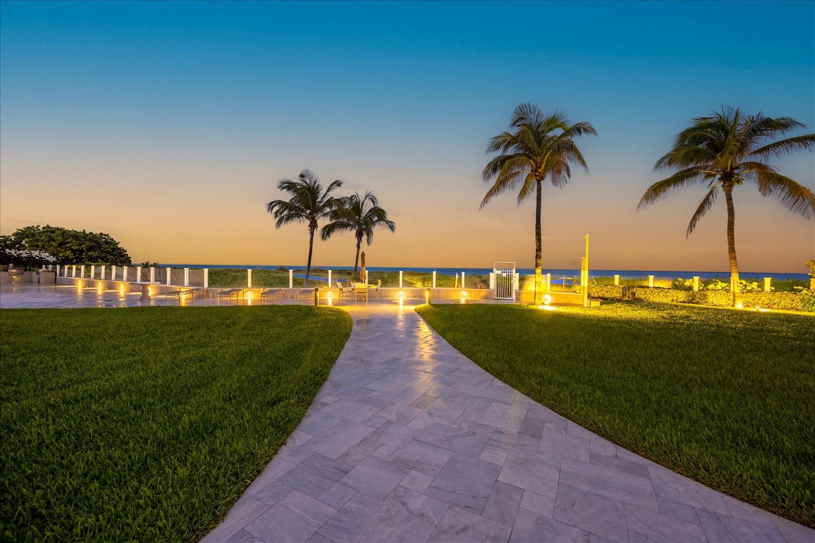 A stone walkway leads through a grassy lawn toward palm trees and an ocean view — 1213 S Ocean Boulevard # e, Delray Beach FL 33483, DELRAY BEACH, FL