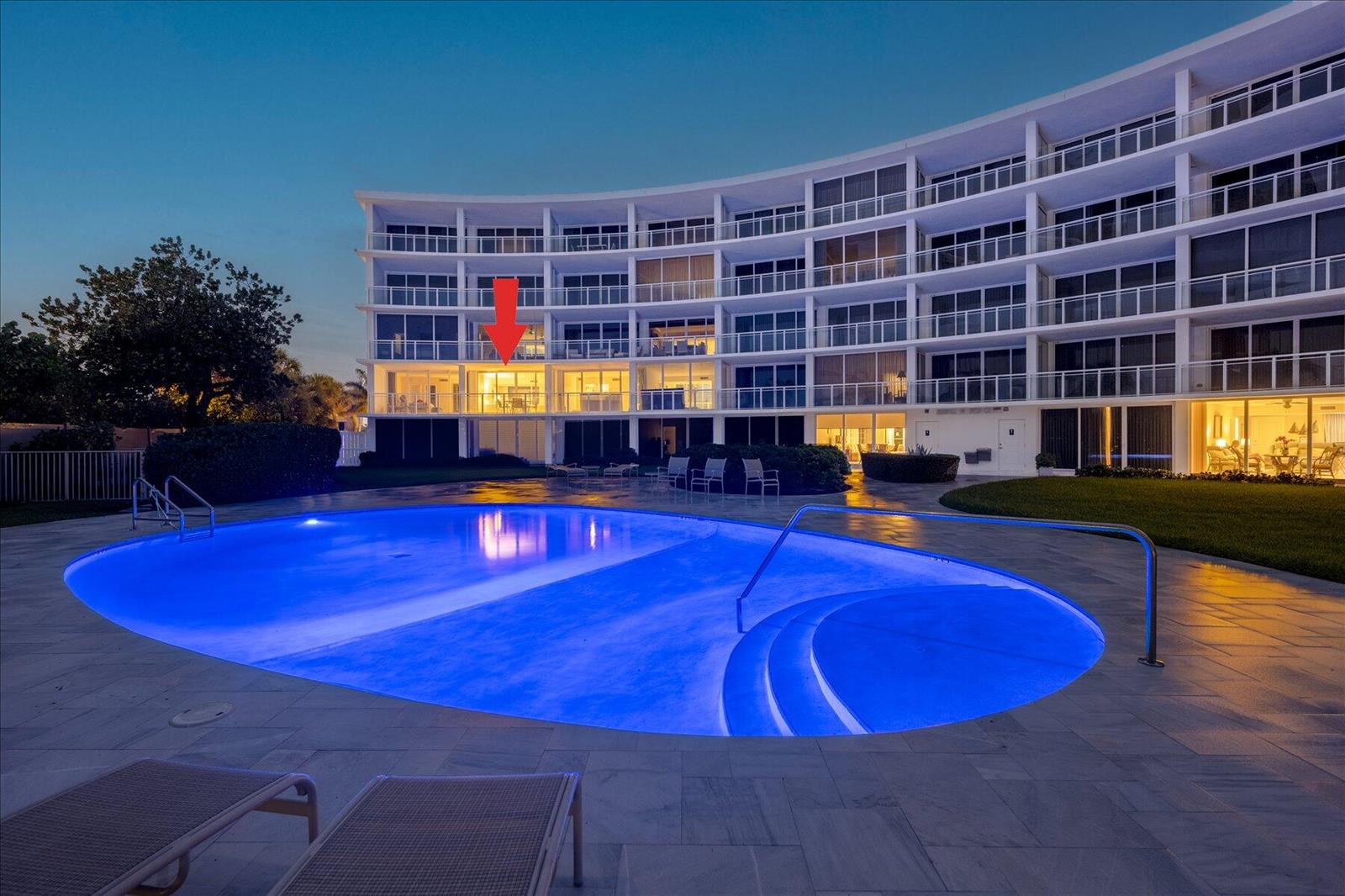 A multi-story curved apartment building overlooks a lit swimming pool at dusk — 1213 S Ocean Boulevard # e, Delray Beach FL 33483, DELRAY BEACH, FL
