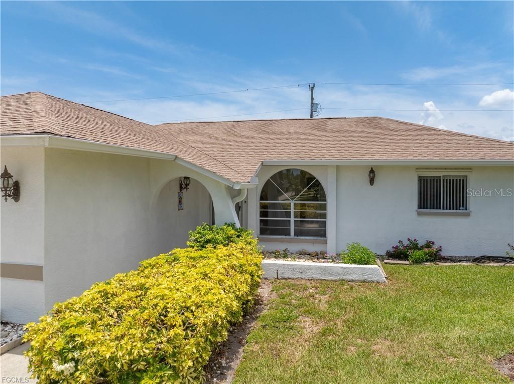 A white house exterior features a tan shingled roof, a front entryway, and landscaping — 1513 SW 44TH STREET, CAPE CORAL, FL
