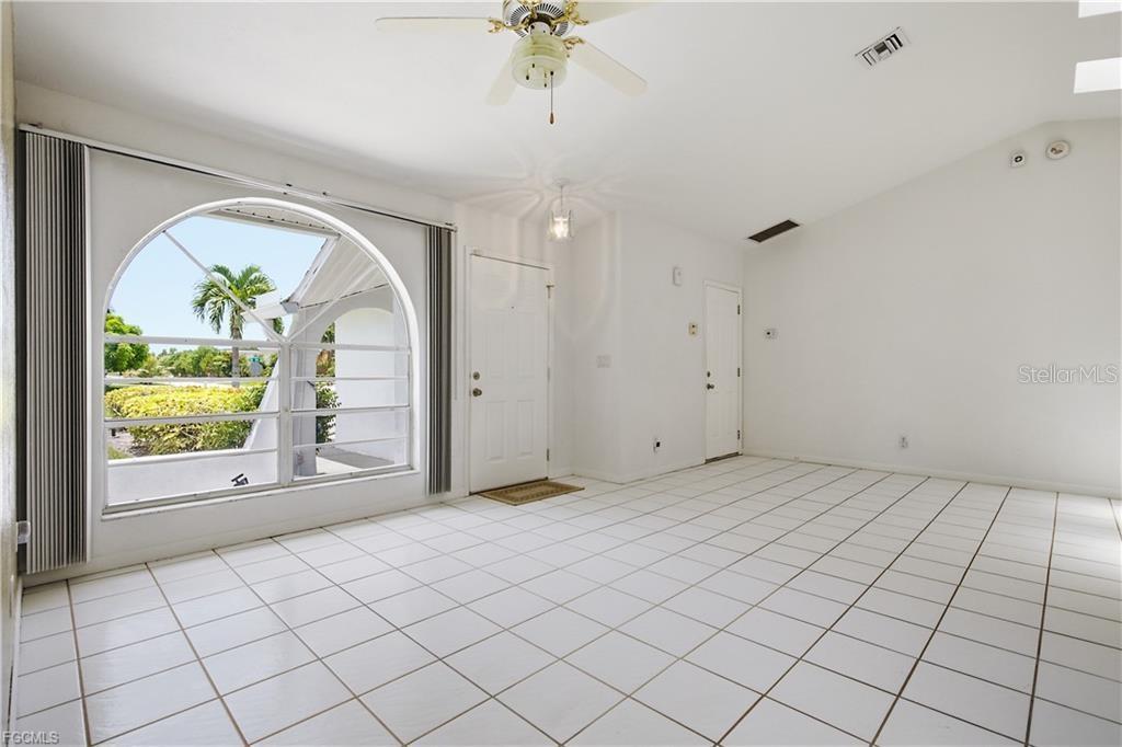 A bright living room features white tile flooring, a vaulted ceiling, and a large arched window — 1513 SW 44TH STREET, CAPE CORAL, FL