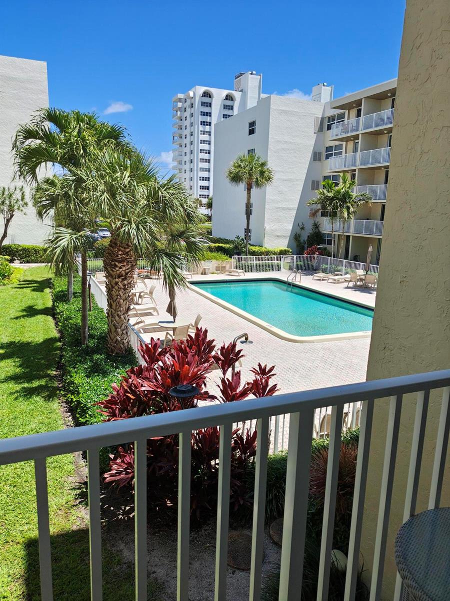 A view from a balcony overlooking a swimming pool surrounded by palm trees and buildings — 2929 S Ocean Boulevard # 2110, Boca Raton FL 33432, BOCA RATON, FL