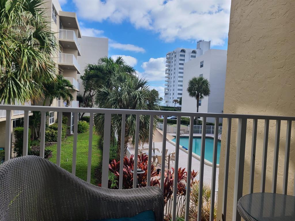 A balcony view overlooking a swimming pool, palm trees, and neighboring apartment buildings — 2929 S Ocean Boulevard # 2110, Boca Raton FL 33432, BOCA RATON, FL