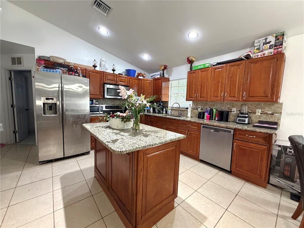 A kitchen features wood cabinets, granite countertops, a center island, and stainless steel appliances — 3510 5TH STREET SW, LEHIGH ACRES, FL