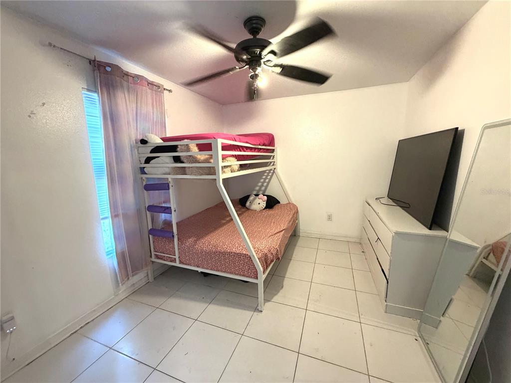 A bedroom features white tile floors, a white metal bunk bed, and a large television — 3510 5TH STREET SW, LEHIGH ACRES, FL